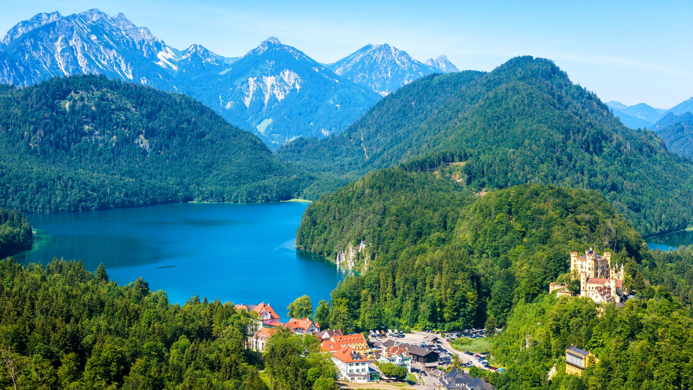 Il castello di Hohenschwangau riflesso nelle acque del lago Alpsee, circondato dalle foreste delle Alpi bavaresi.