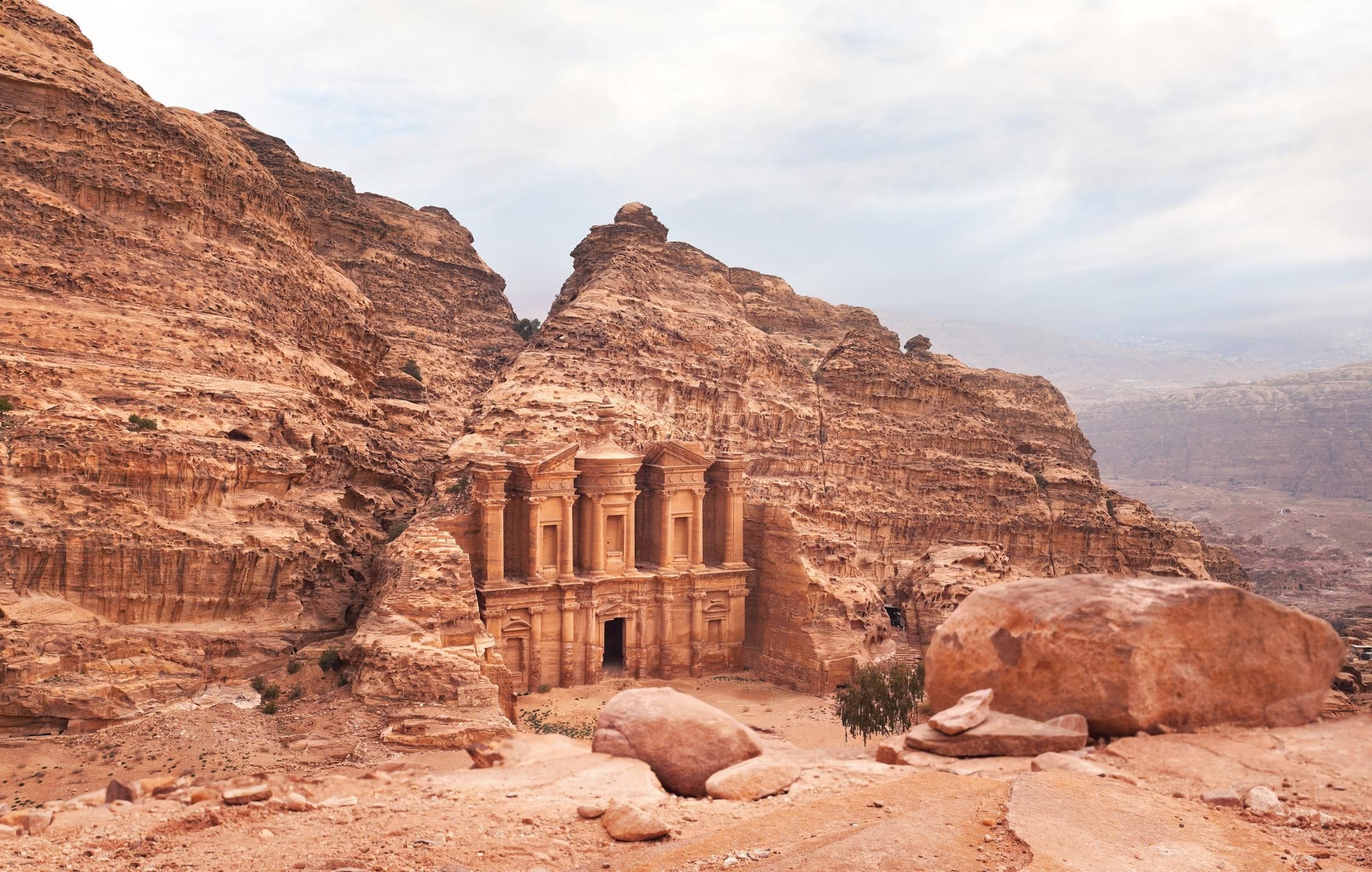 acliviaggi-giordania-wadi-rum-petra-ad-deir-monastery-ruins-carved-rocky-wall-petra-jordan-mountainous-terrain-with-overcast-sky-background-ma